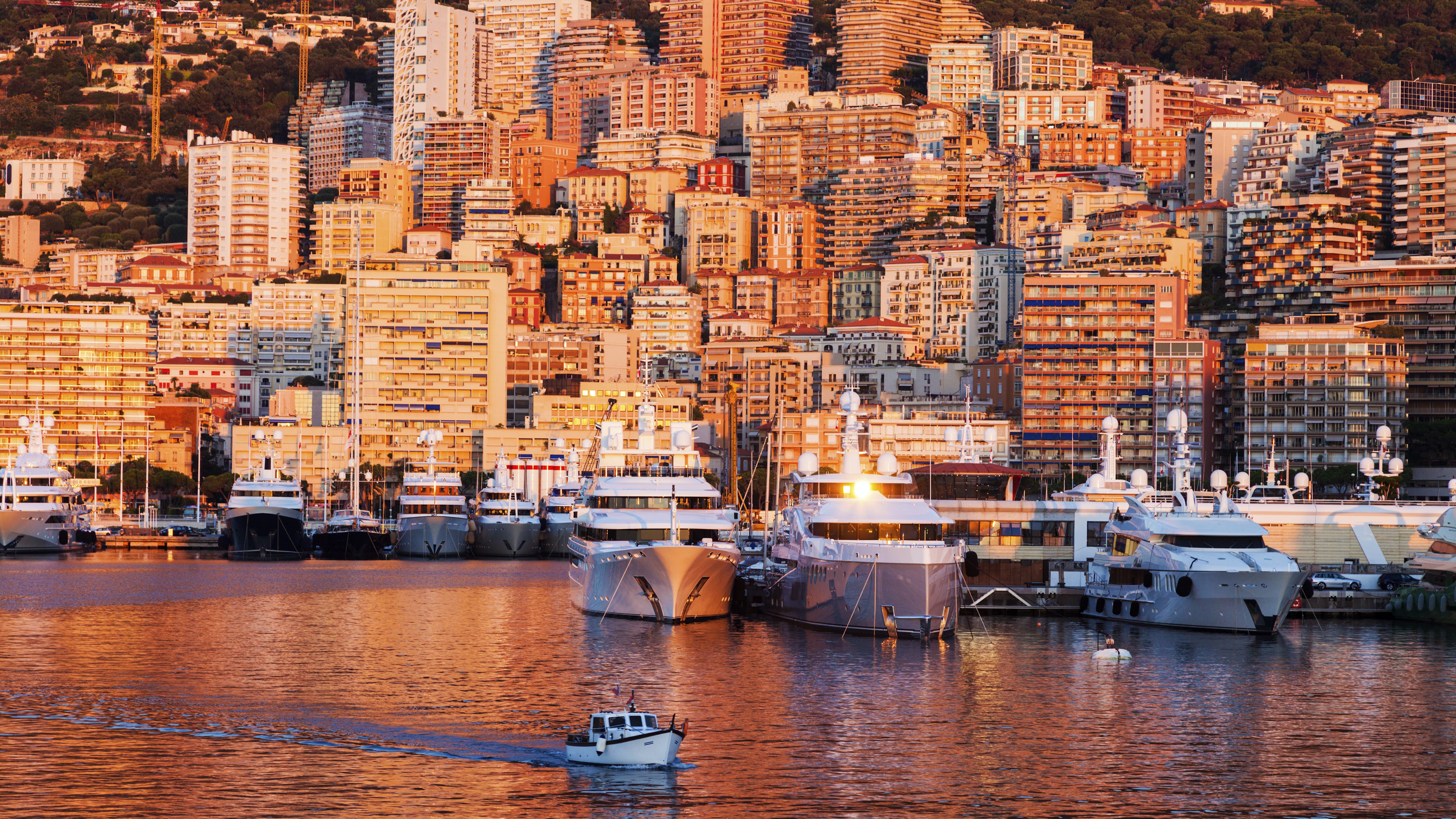 A breathtaking view of Port Hercule in Montecarlo bathed in the warm hues of a sunset, with magnificent superyachts on display during the Monaco Yacht Show.
